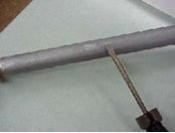 An image of a galvanized pipe with a flathead screwdriver scratching it, demonstrating the scratch test.