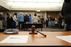 An image of the Newberg City Council chamber centered on the Mayor's gavel with blurry people in the background.