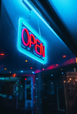 An image of a dark store window with a glowing Open sign hanging in it.